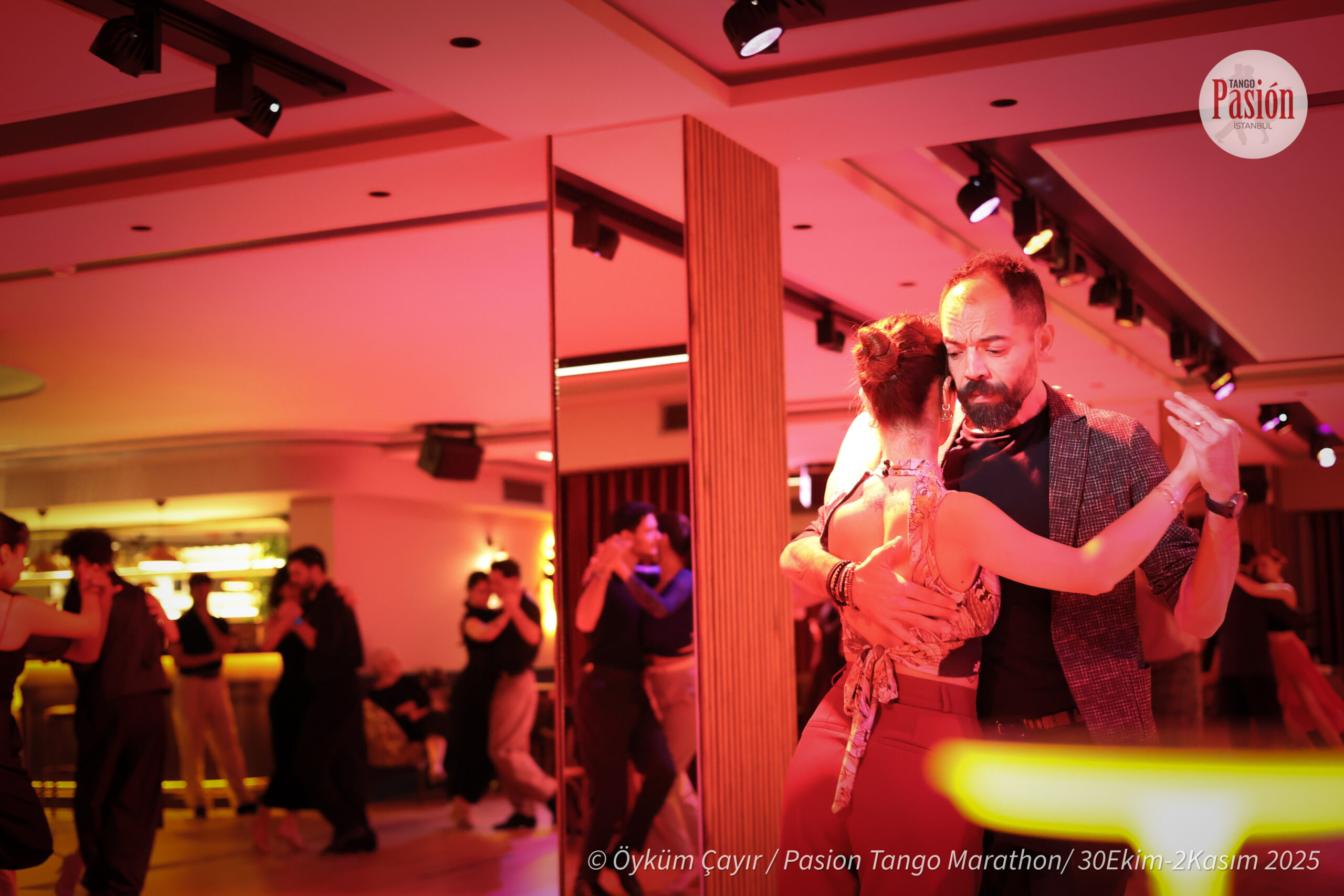 Dancers embracing beside a mirrored column under warm light